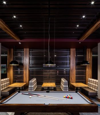 A modern game room with a pool table and wooden booths under hanging pendant lights.