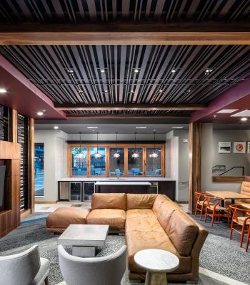 Modern lounge with brown leather sofa, TV, tables, and chairs under a stylish wooden slat ceiling.